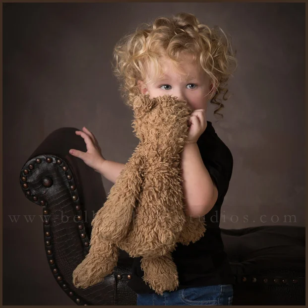 Baby milestone photography portrait of a shy toddler holding his favorite teddy bear. Baby milestone photography portrait of a shy toddler holding his favorite teddy bear.
