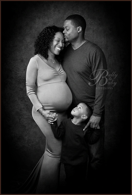 Expecting parents posing with their young child in a black and white maternity portrait Expecting parents posing with their young child in a black and white maternity portrait