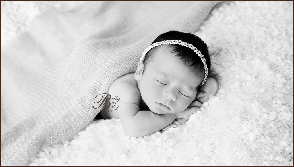 Black-and-white portrait of a sleeping newborn resting on folded hands on a soft textured blanket Black-and-white portrait of a sleeping newborn resting on folded hands on a soft textured blanket