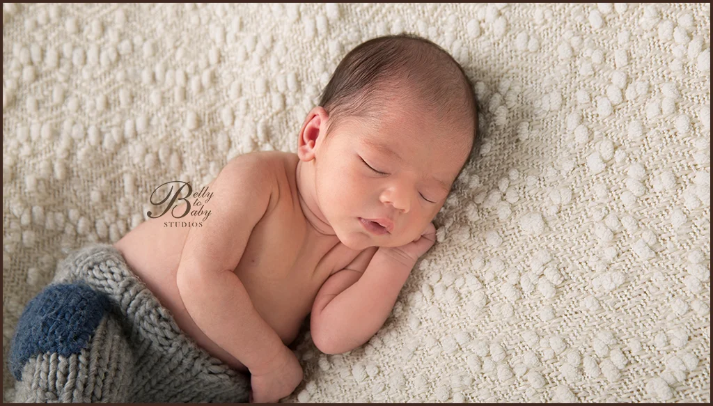 Sleeping newborn boy resting on a cream textured blanket with a blue wrap Sleeping newborn boy resting on a cream textured blanket with a blue wrap