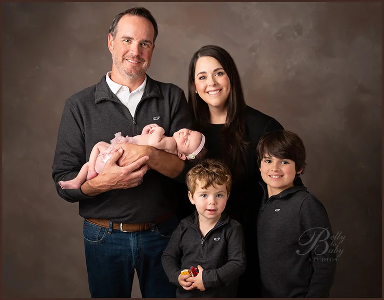 parents holding newborn baby during studio portrait Parents posing with their newborn and two older children for a family portrait